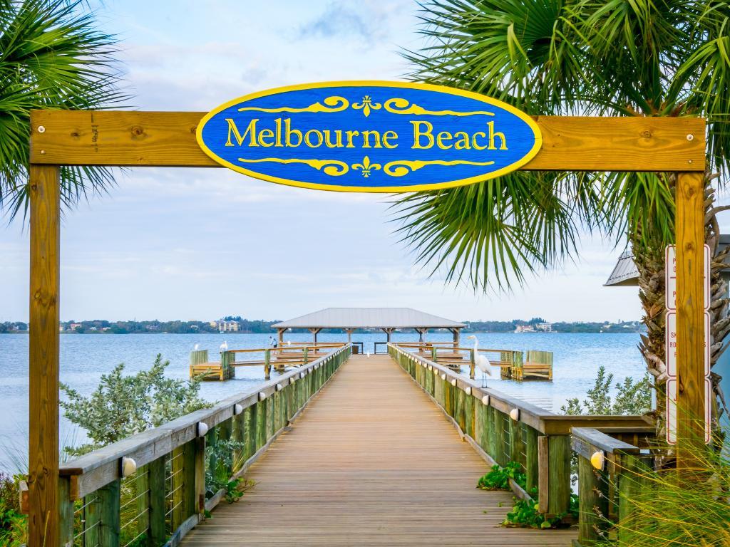 13 Romantic Beaches in Florida Offer the Perfect Couple's Getaway 6 The entrance to Melbourne Beach pier with palm trees on each side and a sign across the top of the pier with the words "Melbourne Beach".