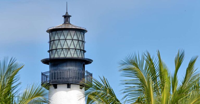 Lighthouses in Florida featured image shows the top of the Cape Florida Lighthouse with its wrought iron detailing and palm fronds on the right side.