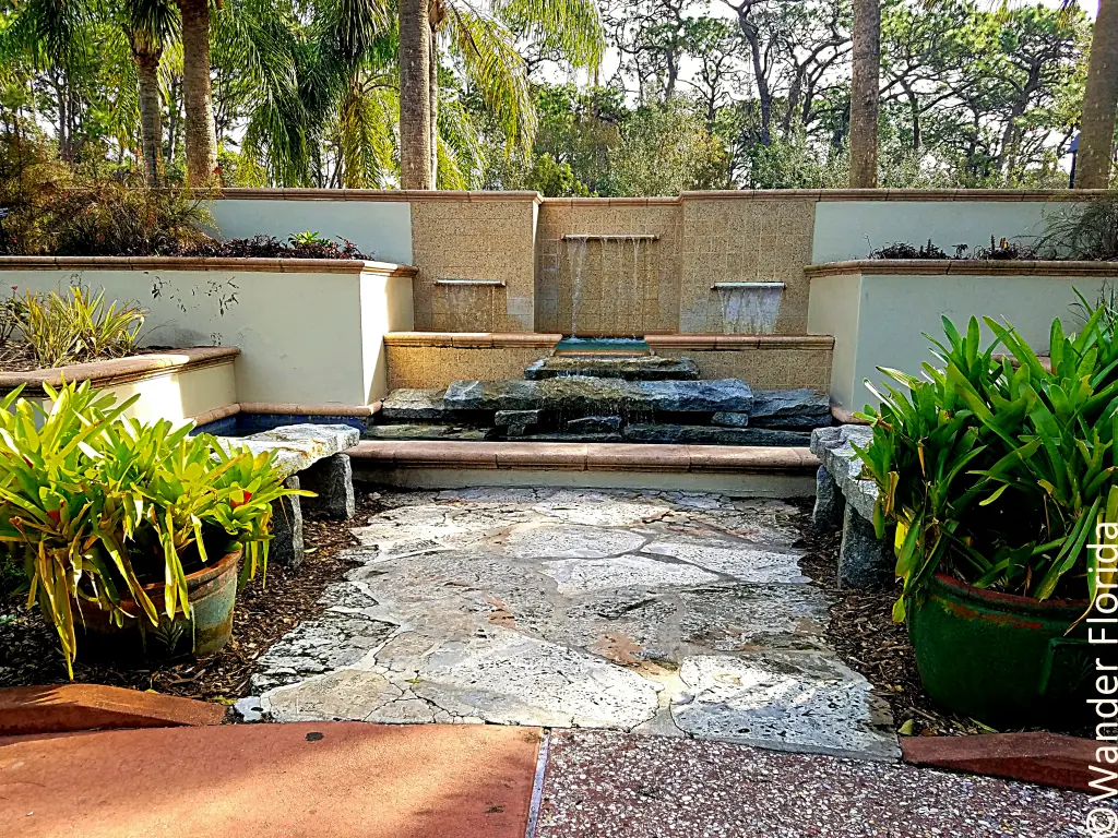 Florida Botanical Gardens - A Beautiful Hidden Gem in Largo 13 A formal water feature in the tropical garden at Florida Botanical Garden features square and rectangular pools, walls, and shelves made from concrete, limestone, and marble with concrete benches on either sie and potted plants lining the gravel walkway leading to the fountain.