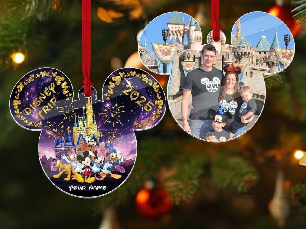 A Christmas tree ornament shaped like Mickey Mouse ears, featuring a vibrant Disney castle and characters on one side labeled "Disney Trip 2025" and a family photo at a theme park on the other, evokes joy and adventure.