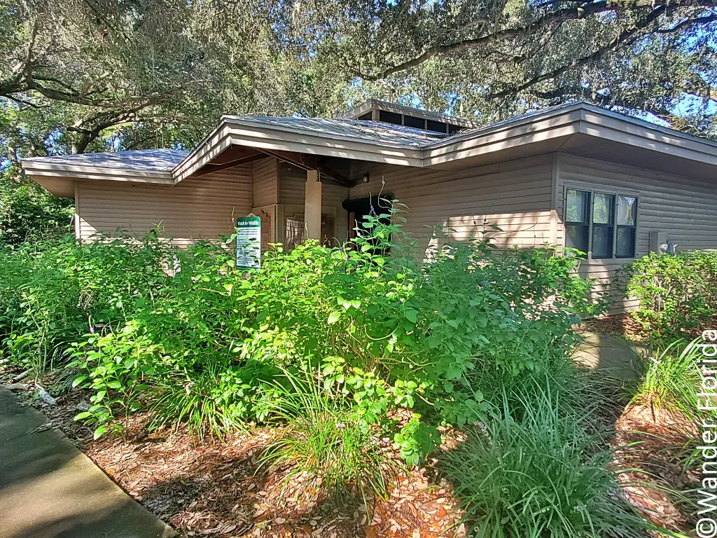 Anderson Environmental Education Center at Sawgrass Lake Park is a single-story brown building surrounded by azaleas, oak trees, and other plants.