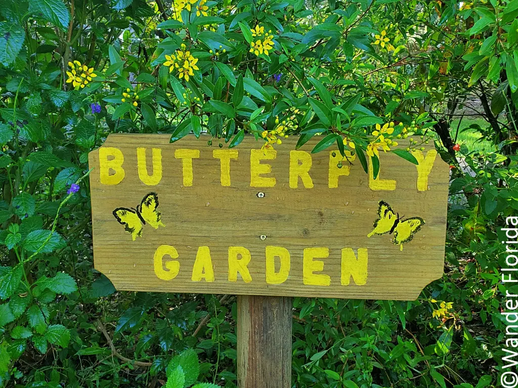 A wooden sign has the words "Butterfly Garden" etched on it and painted in yellow. 