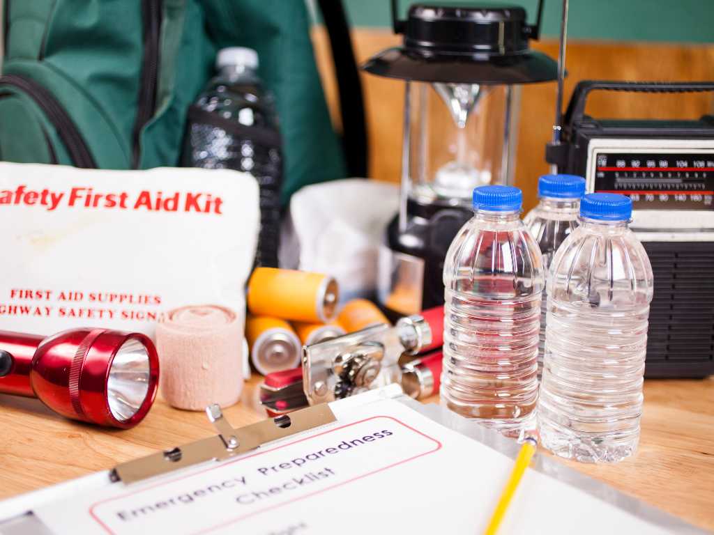 25+ Expert Hurricane Preparedness Tips for Your Home, Family, and Property 3 Water, a flashlight, emergency plan, radio, and other supplies on a counter for hurricane preparedness.