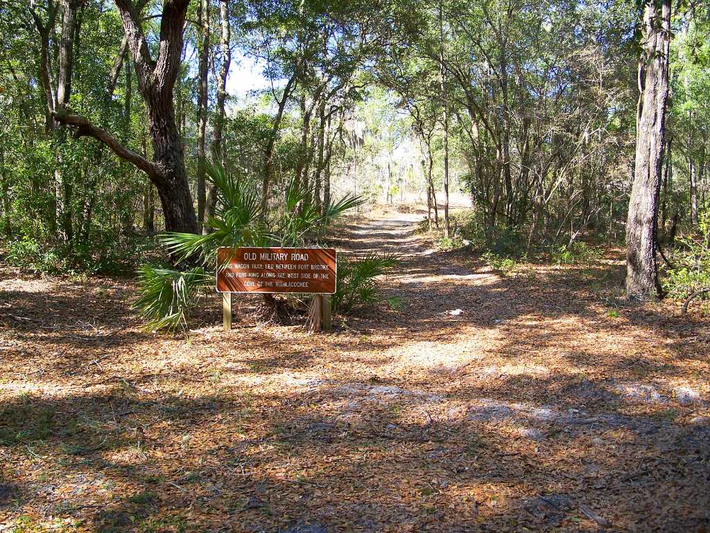 Top 10 Historic Hiking Trails in Florida State Parks 2 A canopy of trees shades a trail with a sign beside it that reads "Old Military Road. This wagon trail led between Fort Brooke and Fort King along the west side of the cove of the Withlacoochee."